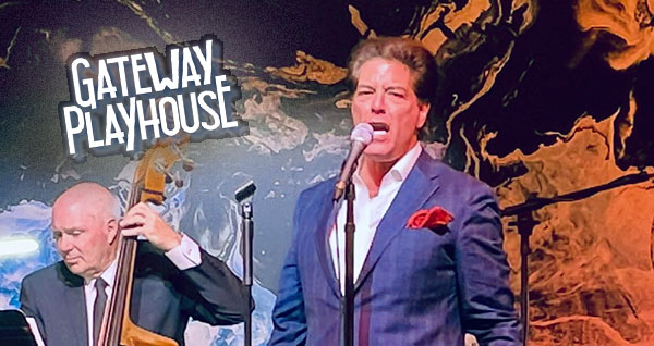 Singer in a blue suit performs at a microphone while a bassist plays upright bass on a dark stage; Gateway Playhouse sign in the background.